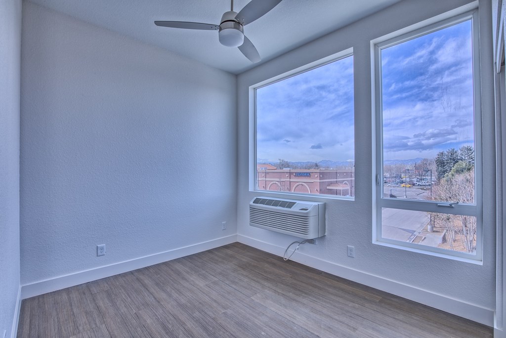A room with a ceiling fan and a window overlooking a cityscape.