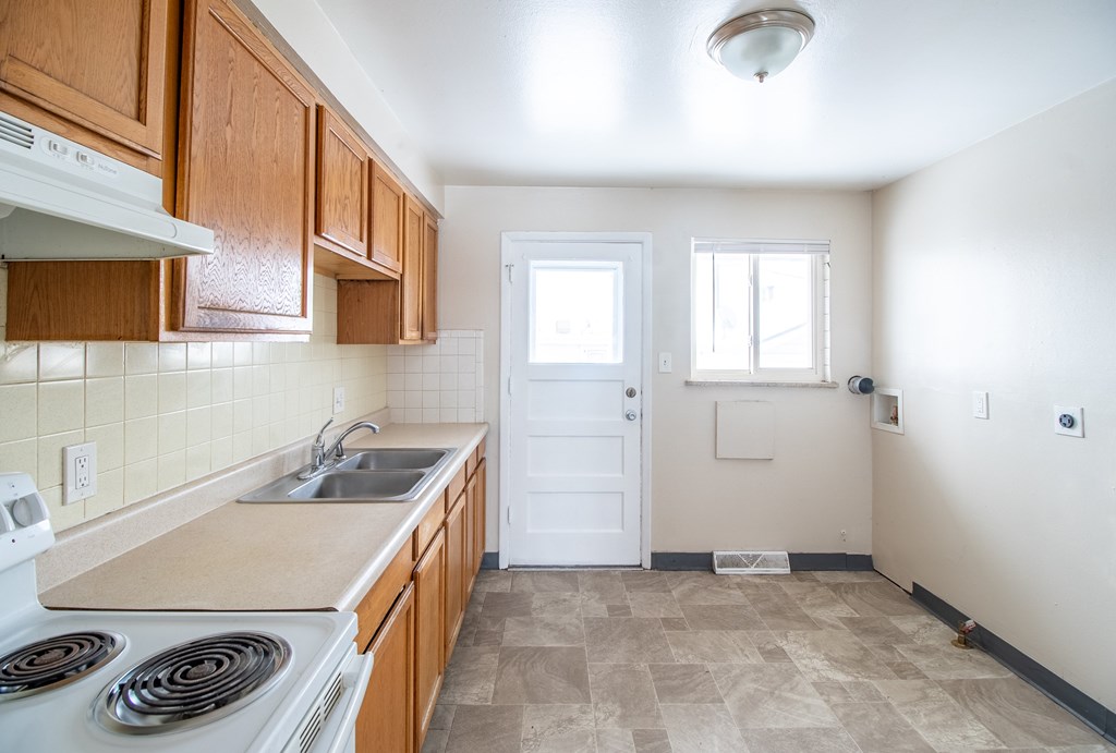 A kitchen with a white stove top oven and wooden cabinets.