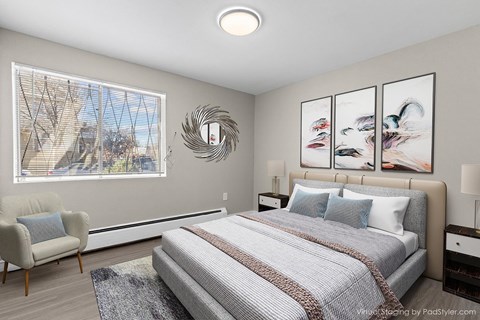 A bedroom with a large bed, a chair, and a window with a view of a tree-lined street.