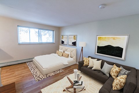 A living room with a brown couch and a white bed.