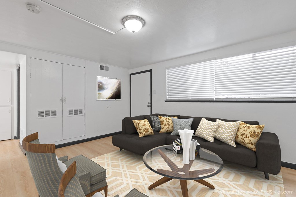 A modern living room with a grey sofa, a glass coffee table, and a wooden chair.
