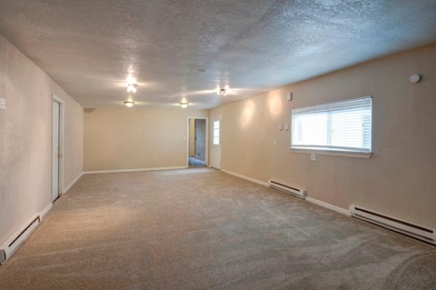 A spacious room with a carpeted floor and a window with blinds.