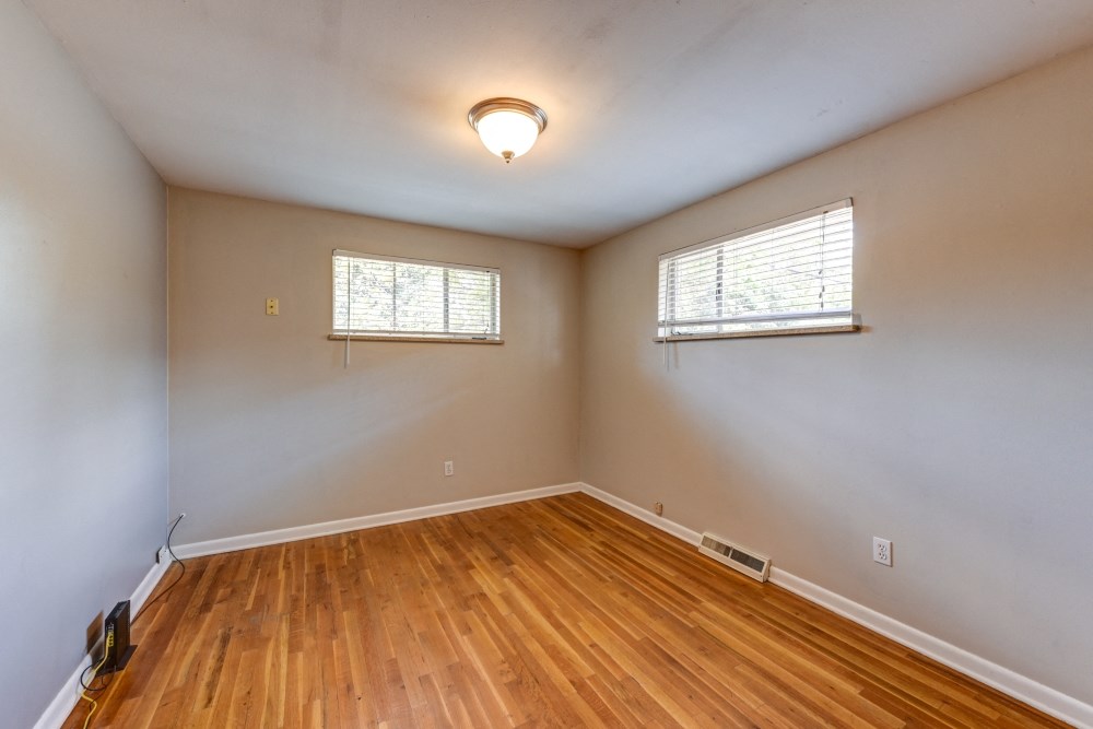 an empty living room with wood flooring and two windows