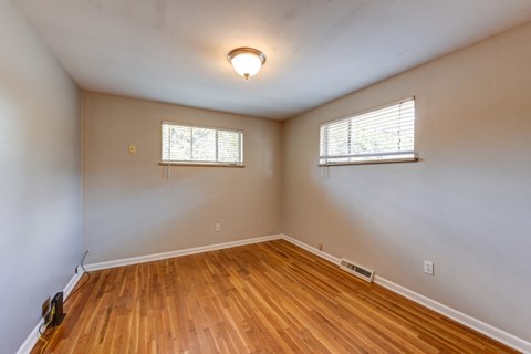 an empty living room with wood flooring and two windows