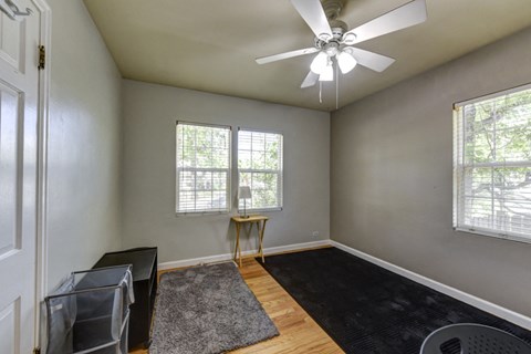 A room with a ceiling fan and two windows.