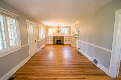 A long, empty room with a fireplace and wooden floors.