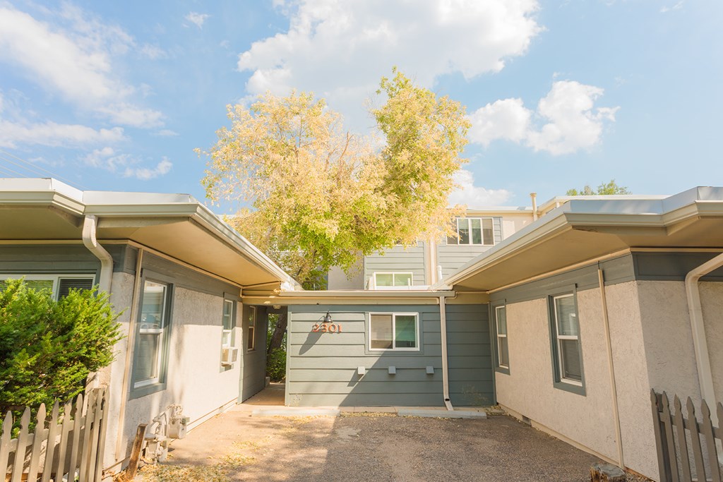 A house with a grey and white exterior and a tree with yellow leaves in the background.