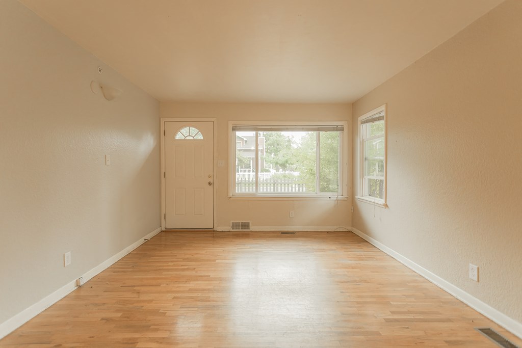 Empty room with wooden floors and a door leading to a balcony.