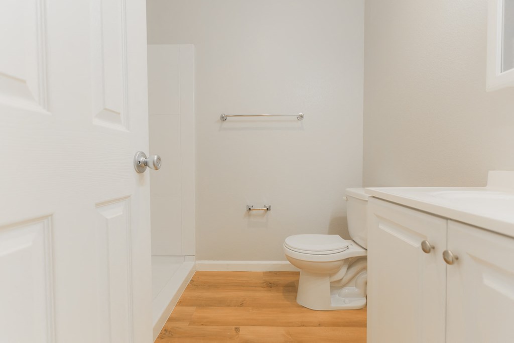A white bathroom with a toilet, sink, and wooden floor.