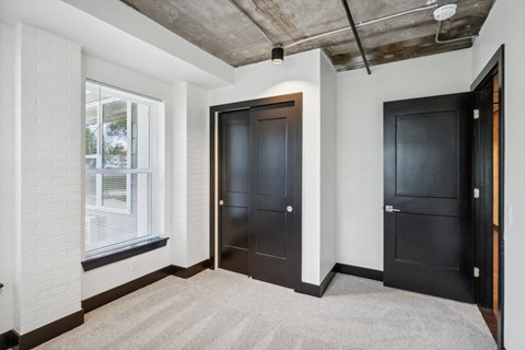 a living room with two black doors and a window and a door to a bedroom