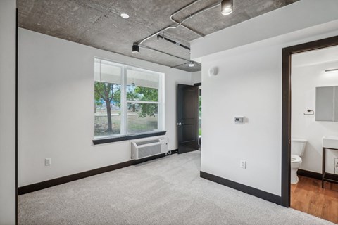 an empty living room with a large window and a door to a bathroom