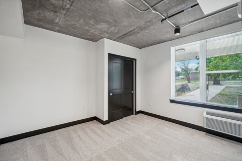 an empty living room with a large window and a door to a hallway