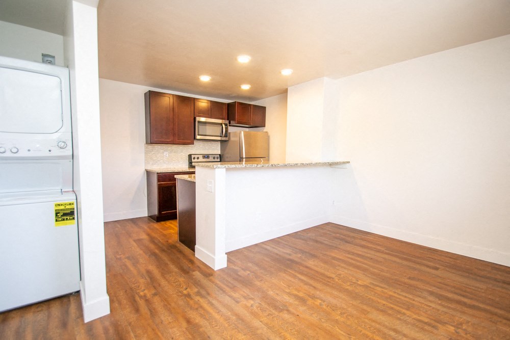 an empty living room with a kitchen and a washer and dryer
