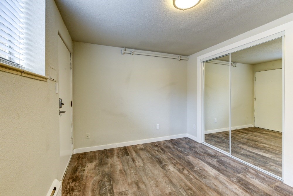 the spacious living room and bedroom of an apartment with a mirrored closet