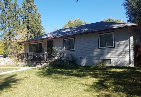 A house with a grey siding and a red roof with a small porch and a tree in the background.