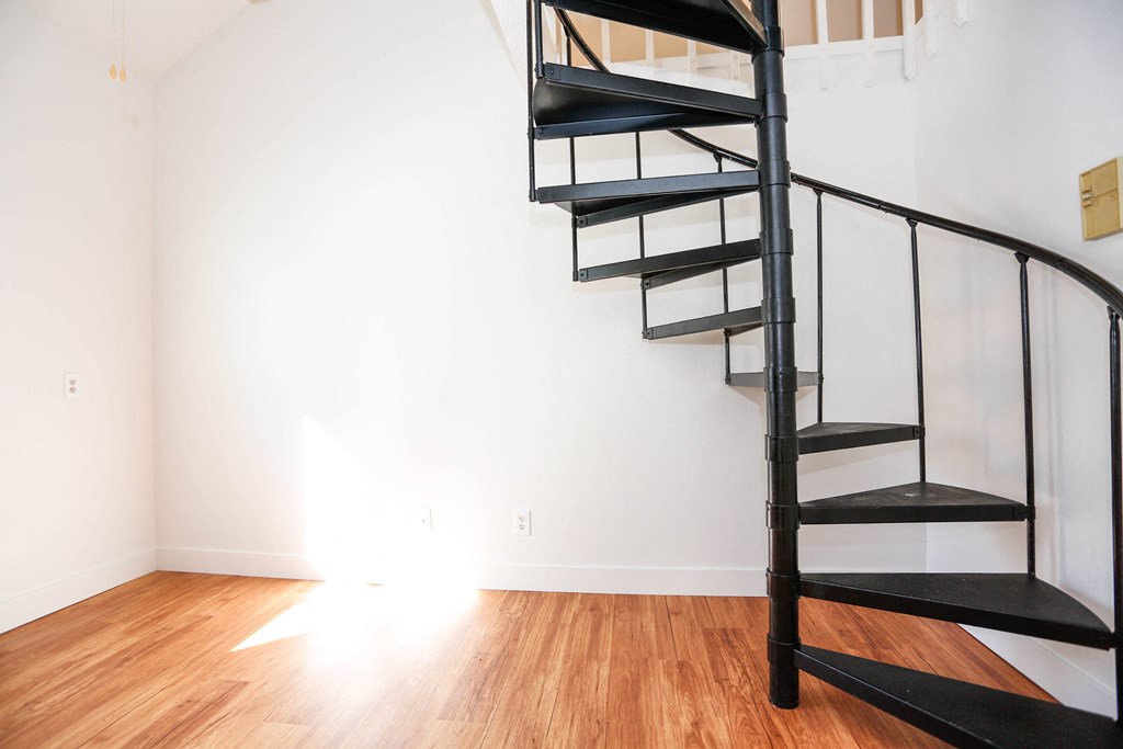 a spiral staircase in a room with a white wall and wooden floors