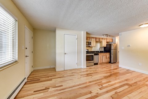 an empty living room with wood floors and a kitchen