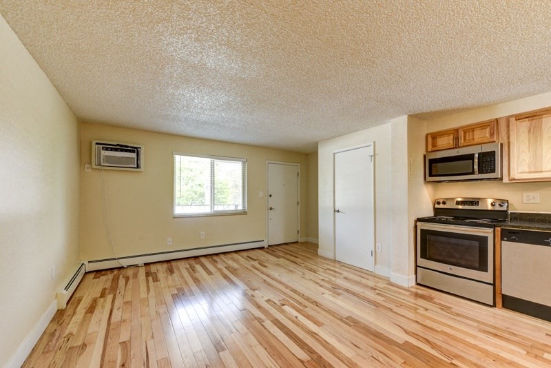 the spacious living room with wood flooring and an empty kitchen with appliances