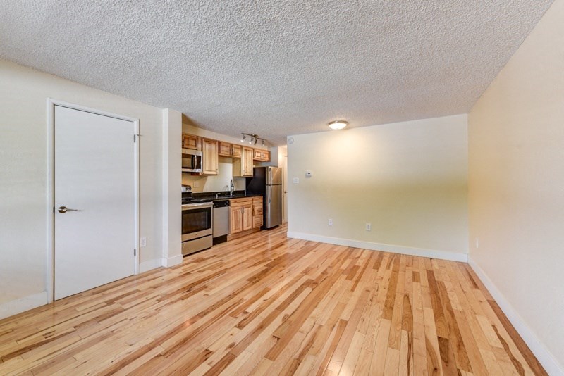 an empty living room with wood flooring and a kitchen