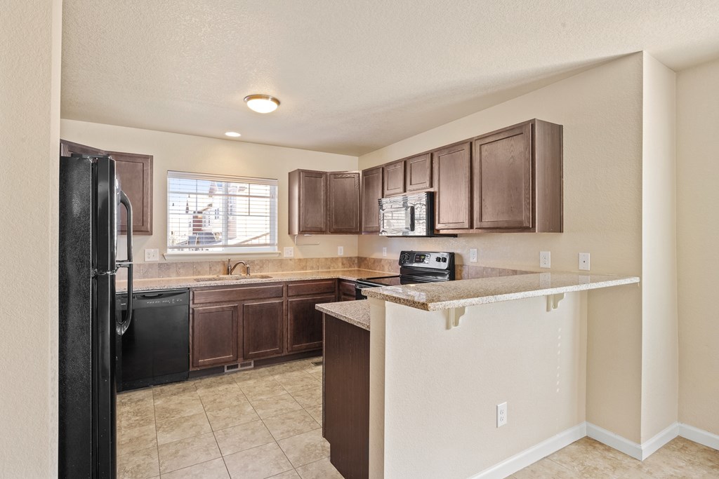 A kitchen with brown cabinets and a black refrigerator.
