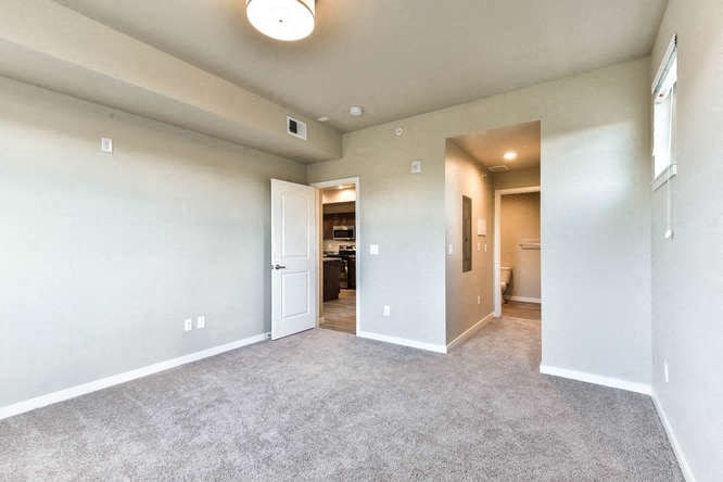 an empty living room with a door to a kitchen