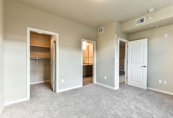 an empty living room with open doors to a bedroom and a bathroom