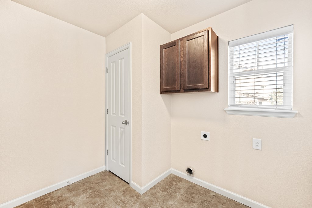 A room with a white door, a window with blinds, and a brown cabinet above the door.