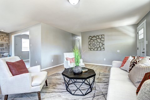 A living room with a white couch, a chair, and a table with a vase on it.