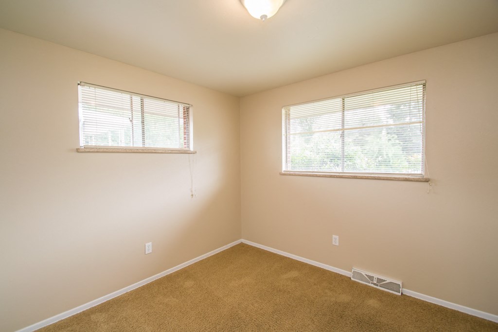 an empty room with two windows and a carpet