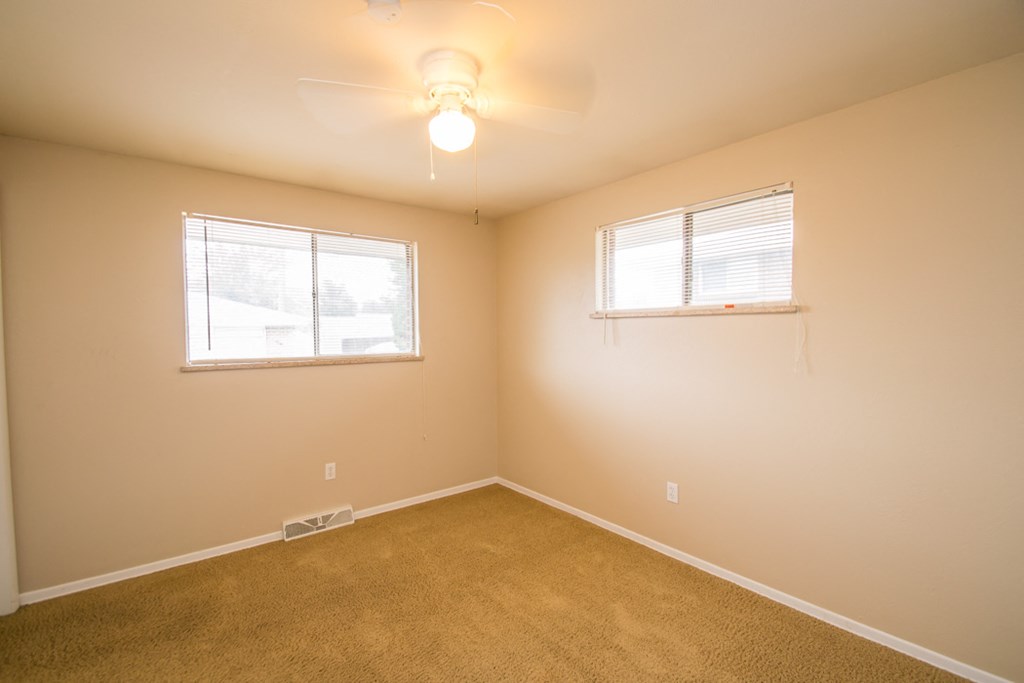 an empty bedroom with a ceiling fan and two windows