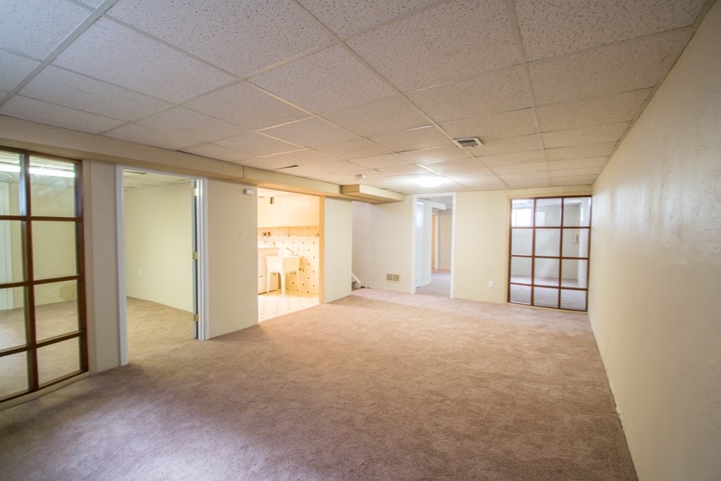 the living room and kitchen of an empty house with a carpeted floor and windows