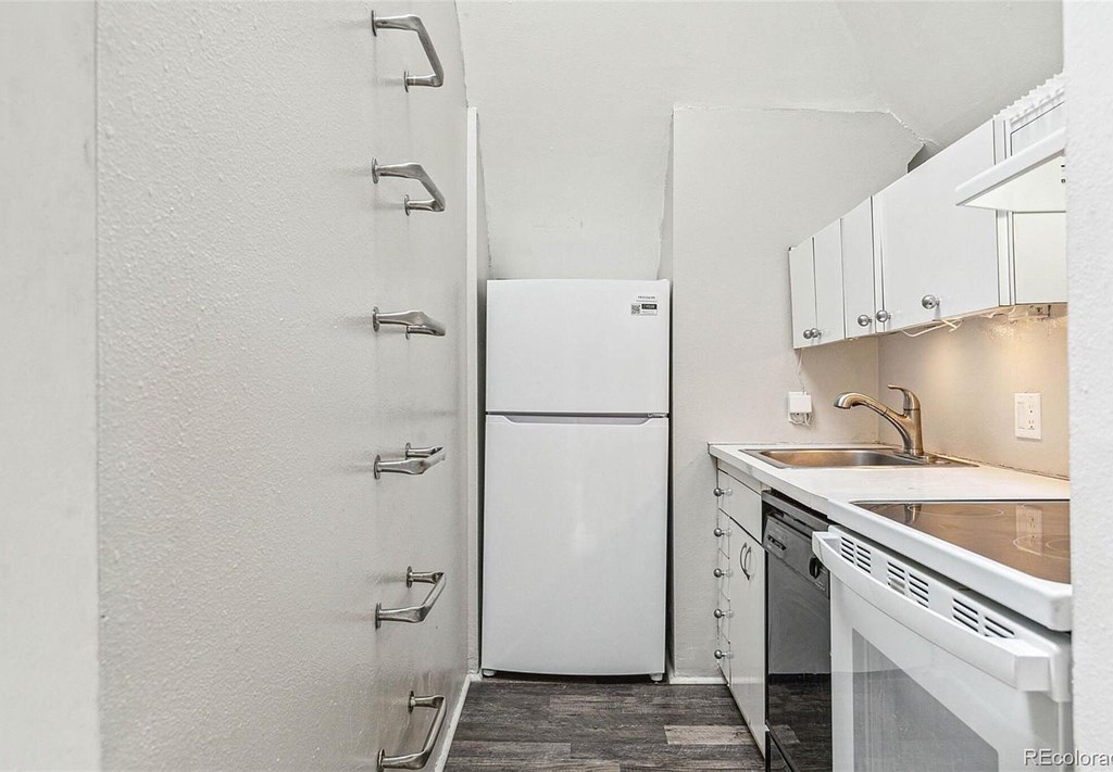 A white refrigerator in a kitchen with white cabinets.