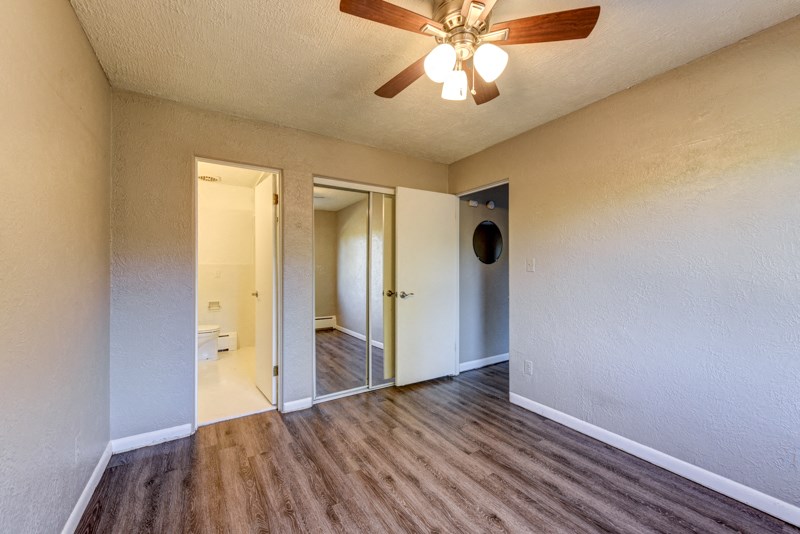 an empty living room with a ceiling fan and a door to a bathroom