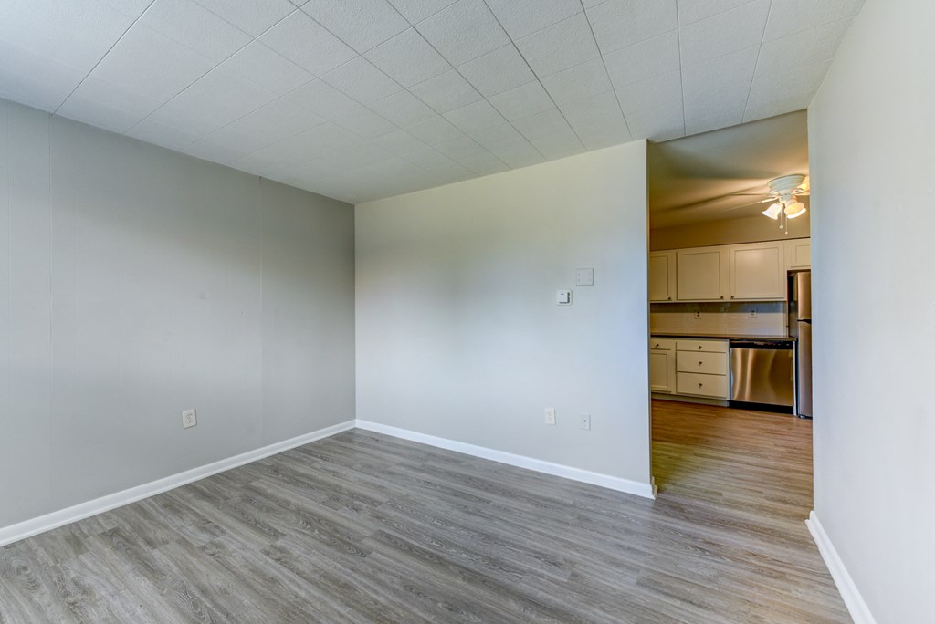 an empty living room and kitchen with wood floors and white walls