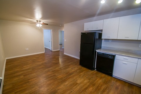 an empty living room with a kitchen and a black refrigerator