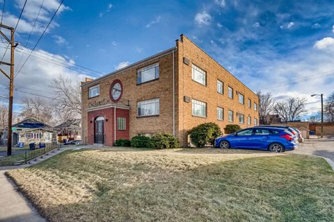 A blue car is parked in front of a brick building with a red circle on the front.