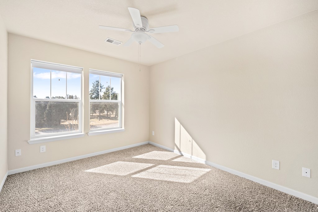 A room with a ceiling fan and two windows.