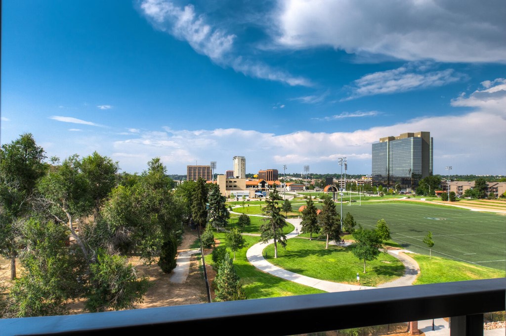 A view of a cityscape from a balcony with buildings, trees, and a clear sky.at Peregrine Place Apartments, Denver, CO 80246