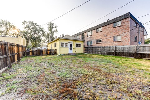 A backyard with a yellow building and a red brick building.