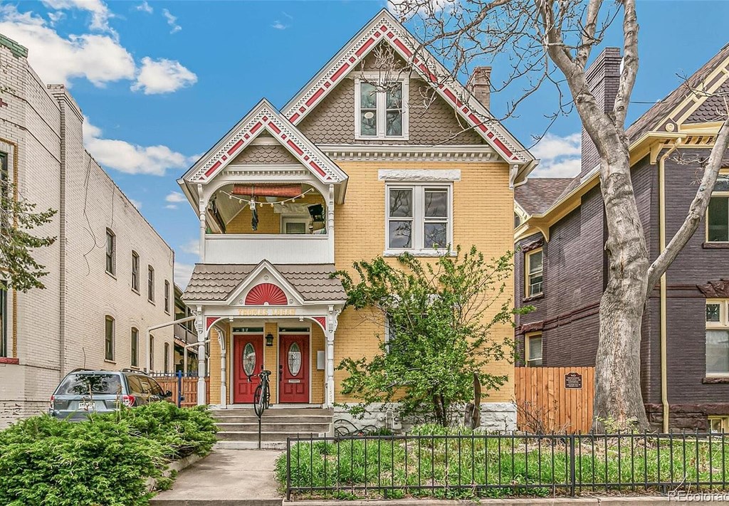 A yellow house with a red door is in front of a grey house.