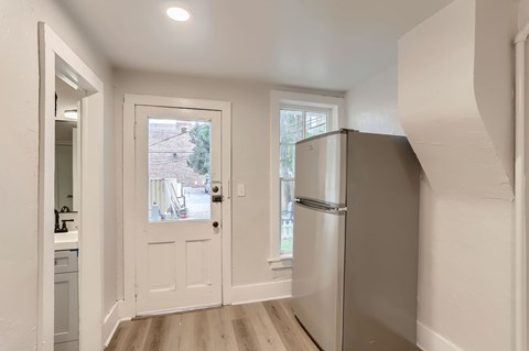 A white door is open to a kitchen and a window is in the background.
