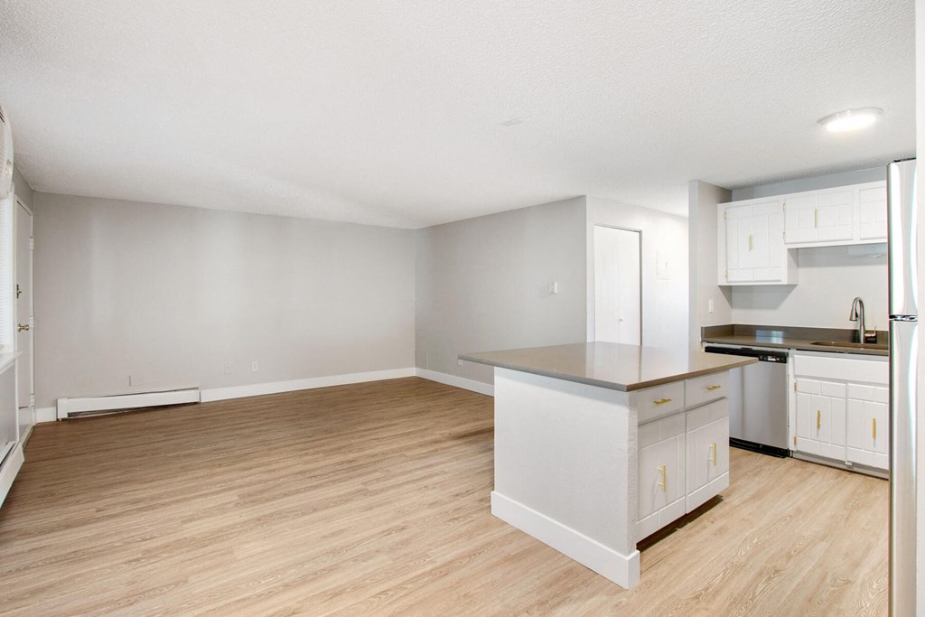 an empty kitchen and living room with wood flooring and white cabinets