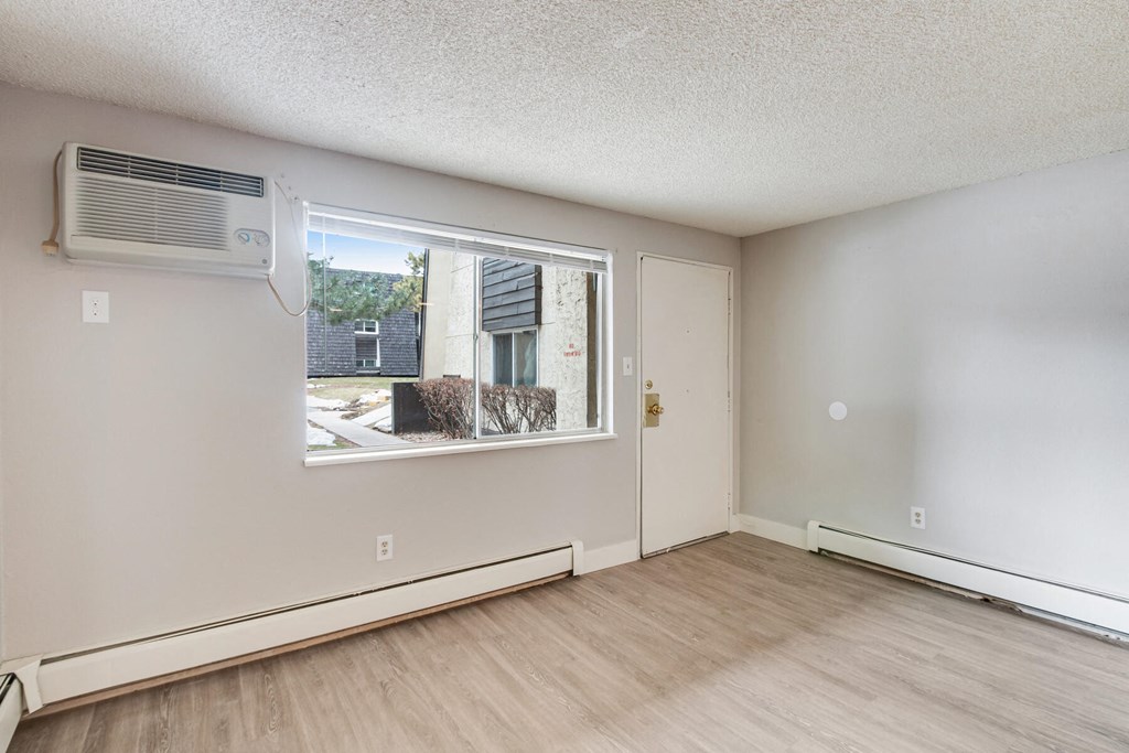 an empty living room with a window and a air conditioner