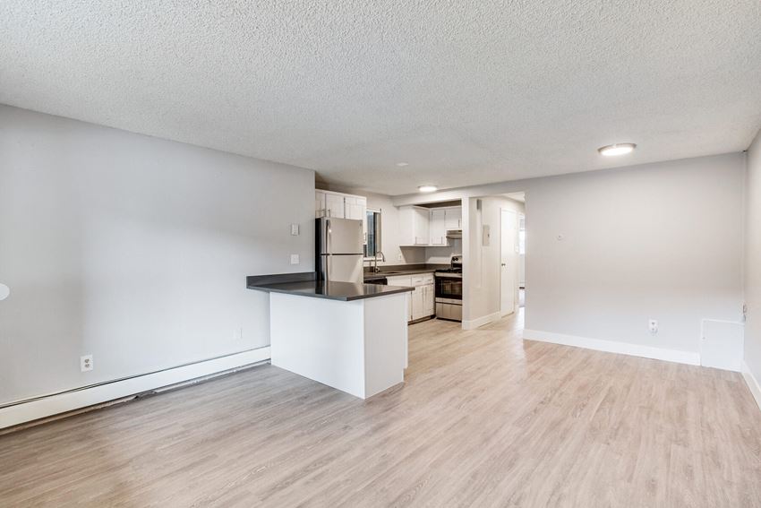 the living room and kitchen of an apartment with a hardwood floor and white walls