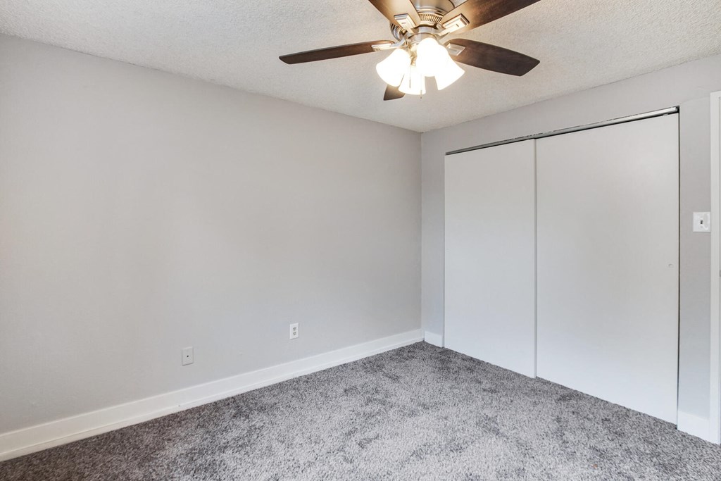 an empty bedroom with a ceiling fan and white closets