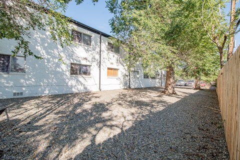 A white building with a brown door is surrounded by trees and a gravel driveway.