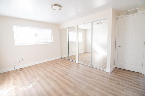 A room with a white door, a window, and a wooden floor.