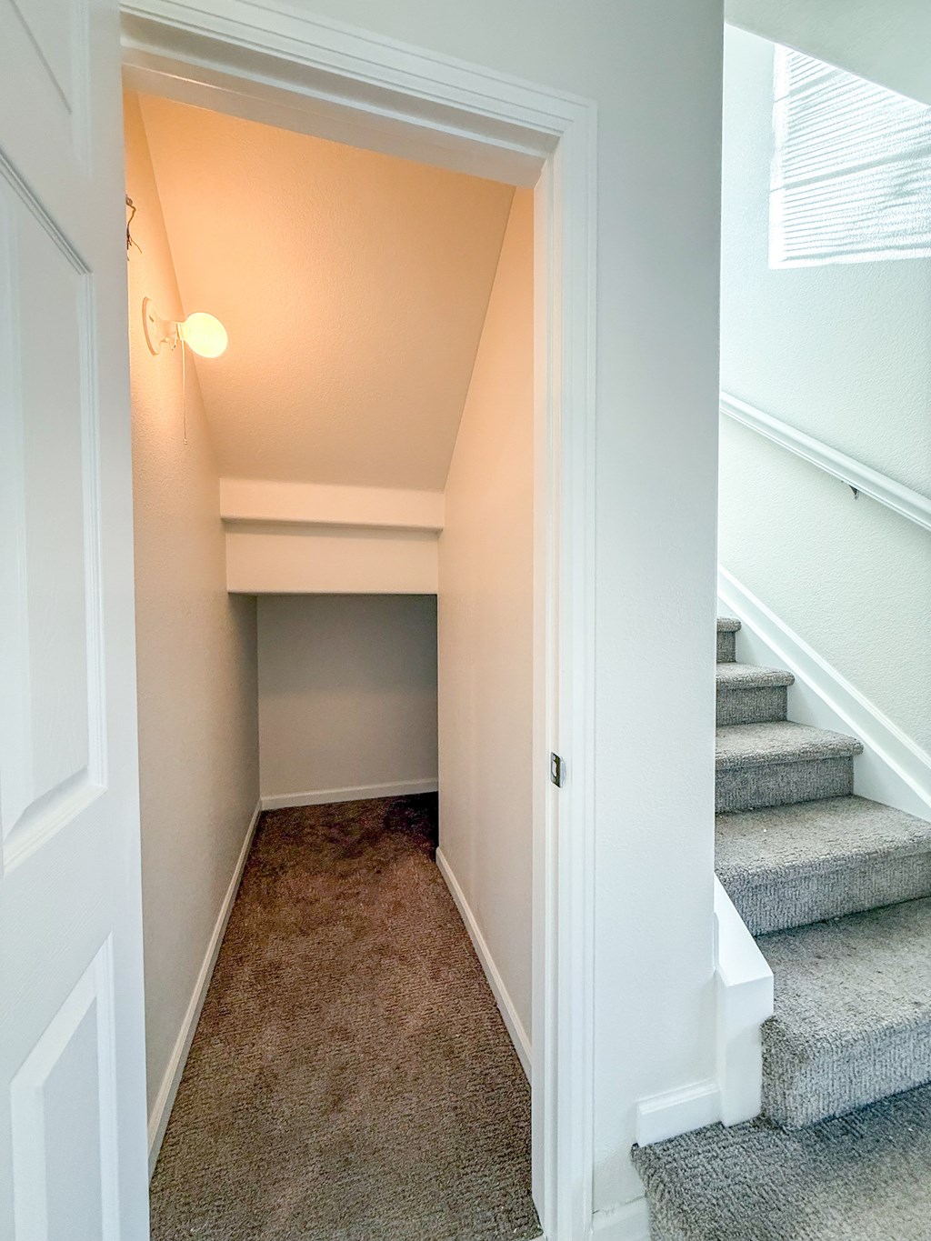 A hallway with a staircase and a light on the wall.