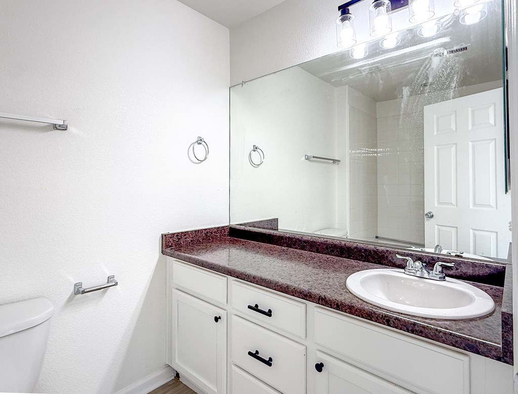 A bathroom with a marble countertop and white cabinets.