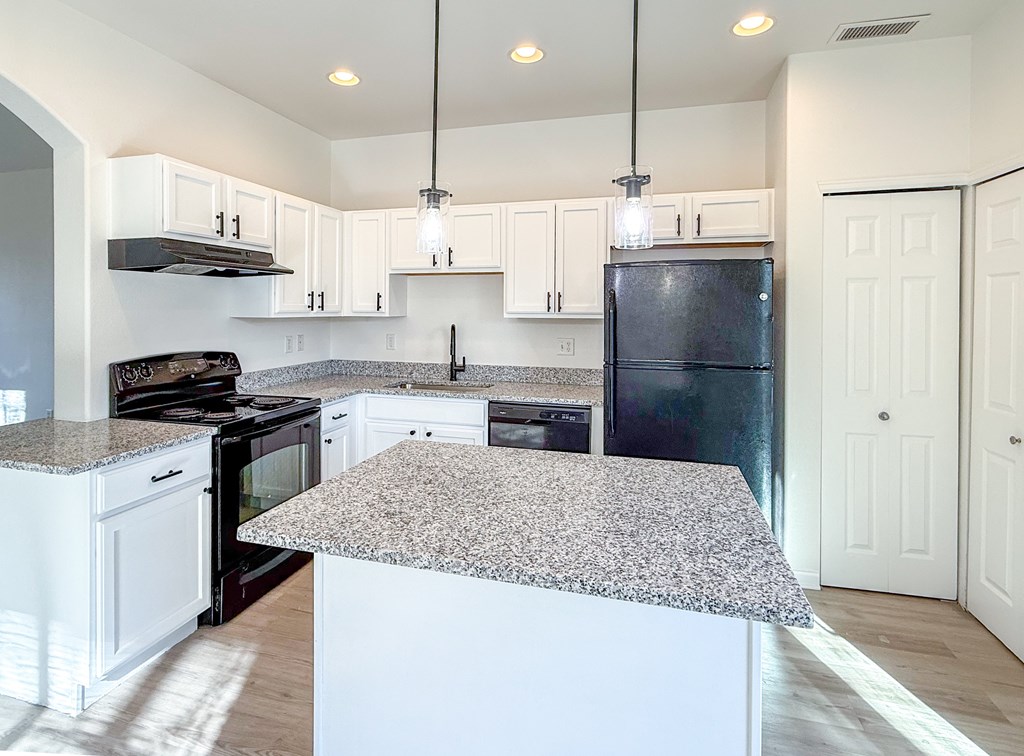 A kitchen with a granite countertop and a black refrigerator.